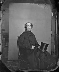 En man sitter på en stol med cylinderhatt (storm) i knät Tro