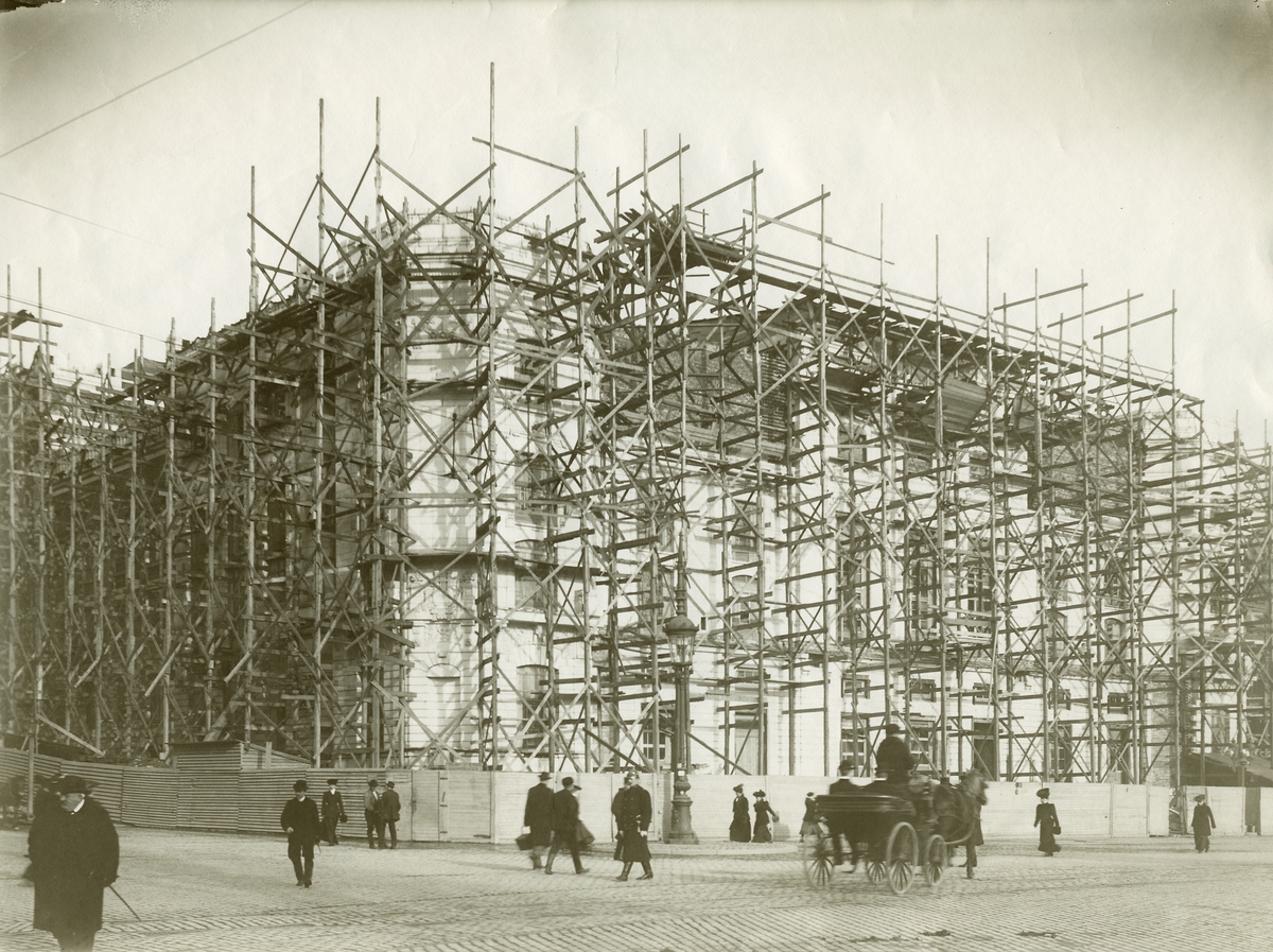 Foto från byggnationen av Dramatens jugendinspirerade nybyggnad (1901-1908) vid Nybroplan i Stockholm.
Byggnaden blev färdig 1908.Byggherre var Per Axel Ludvig Lindahl (1858-1934) civilingenjör, byggnadskonstruktör och överstelöjtnant vid Väg- och vattenbyggnadskåren.
Bild tagen 6 mars 1906.