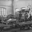 Ljusbild gällande tillverkning av aluminium och lättmetall i slutet av 1920- talet. Två män vid press i verkstad.