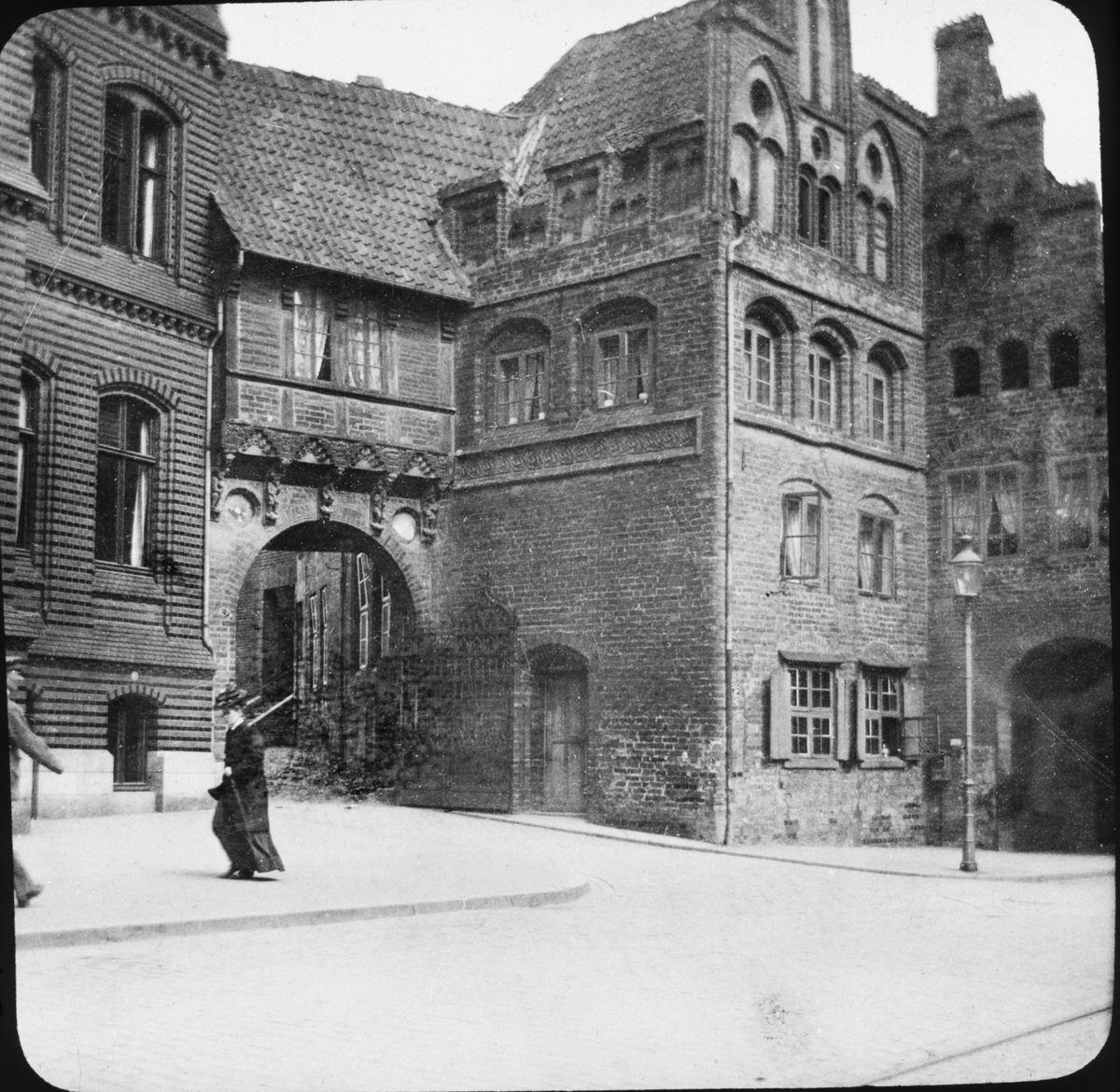 Skioptikonbild med motiv av kvinna vid Lübecker Burgtor (slottsporten) i Lübeck.
Bilden har förvarats i kartong märkt: Resan 1907. Lübeck 3. Braunschweig 5. 3.