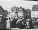 Skioptikonbild med motiv av folksamling på marknad på Hauptmarkt i Nürnberg.
Bilden har förvarats i kartong märkt: Resan 1907. Bamberg 2. Nürnberg 6. 295. Text på bild: 