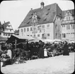 Skioptikonbild med motiv av marknad framför rådhuset i Heilbronn.
Bilden har förvarats i kartong märkt: Resan 1908. Heilbronn 4. Wimpfen 5.