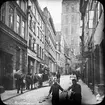 Skioptikonbild med motiv av pojkar med cykel samt man med häst och kärra på Schüsselbuden i Lübeck, i bakgrunden St. Marien Kirche.
Bilden har förvarats i kartong märkt: Lybeck 1903