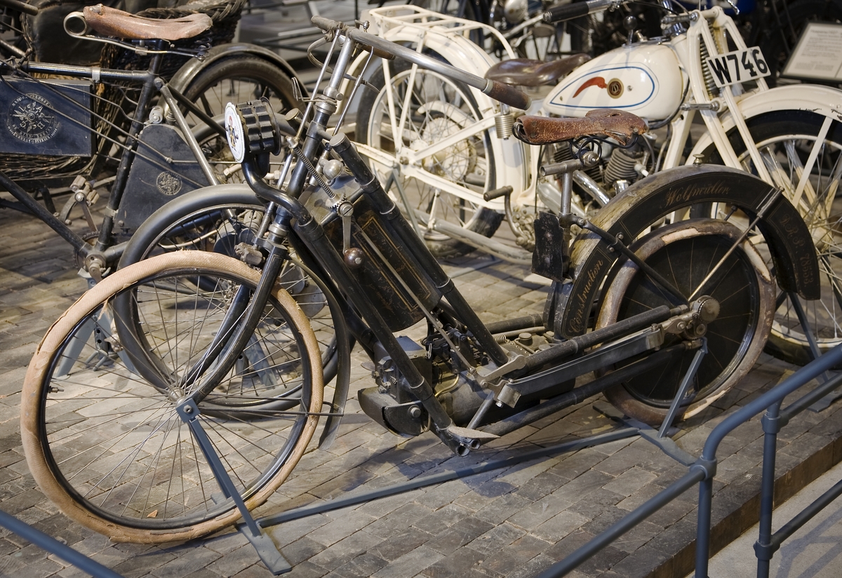 Liggande bensinmotor i en ram som tillverkningstekniskt sett liknar samtida cyklars. Vevstakarna överför kraften till vevarna på bakhjulet som även fungerar som svänghjul. För utväxlingen är bakhjulets diameter 22 tum, framhjulet är 26 tum. Ytförgasare i bensintanken, bränsle-luftblandningen antänds av ett glödrör av nickel som upphettas av en bensinblåslampa. Vattentanken ligger i den bakre stänkskärmen. Tillverkningsnummer sannolikt  509.  Tvåcylindrig vattenkyld fyrtaktsmotor, cylindervolym 1488 cc Cylinderdiameter: 90 mm Slaglängd: 117 mm 2,5 hk vid 240 varv/minut Högsta fart, enligt prospekt, 60 km/tim Vikt med bensin och vatten cirka 60 kg Däckdimension: Fram: Vulst 25 x 1 1/2. Bak: Vulst 20 x 1
