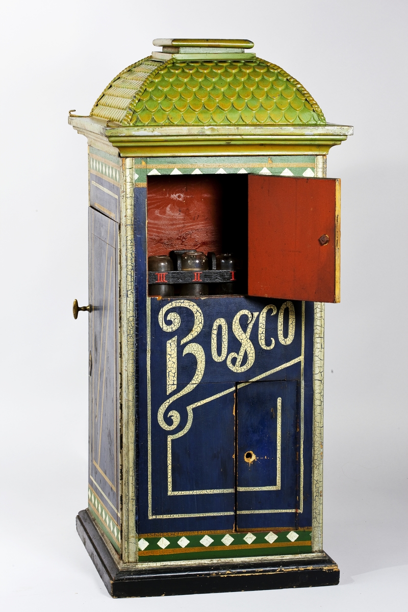 Fotoautomat "Bosco" för tillverkning av ferrotypier. Penningautomat för självfotografering.  Den fungerade på så sätt att det ljuskänsliga skiktet placerats i en profilerad plåtbricka som på samma gång var framkallningsskål och sedan ram för fotografiet. I automaten exponerades bilden i lodrätt läge och framkallades sedan med vätskor som portionerades ur behållare. Efter tre minuter var ferrotypen klar och matades ut ur apparaten. Den behövde torka ytterligare och fick enligt anvisningarna inte utsättas för starkt ljus förrän den var torr. Bilden mätte 60x83 mm och levererades i ett etui av papper. Plåtbrickan hade påtryck av reklam och information på baksida och kanter.
Tillbehör: Sockel med 2 st. metallådor för plåtar, 10 st. plåtar ("W.H.C Bernitt Original Bosco Platte Hamburg 23 ...), överdel med kamera, mekanism, mekanism för framkallning m.m. nyckel till verket.