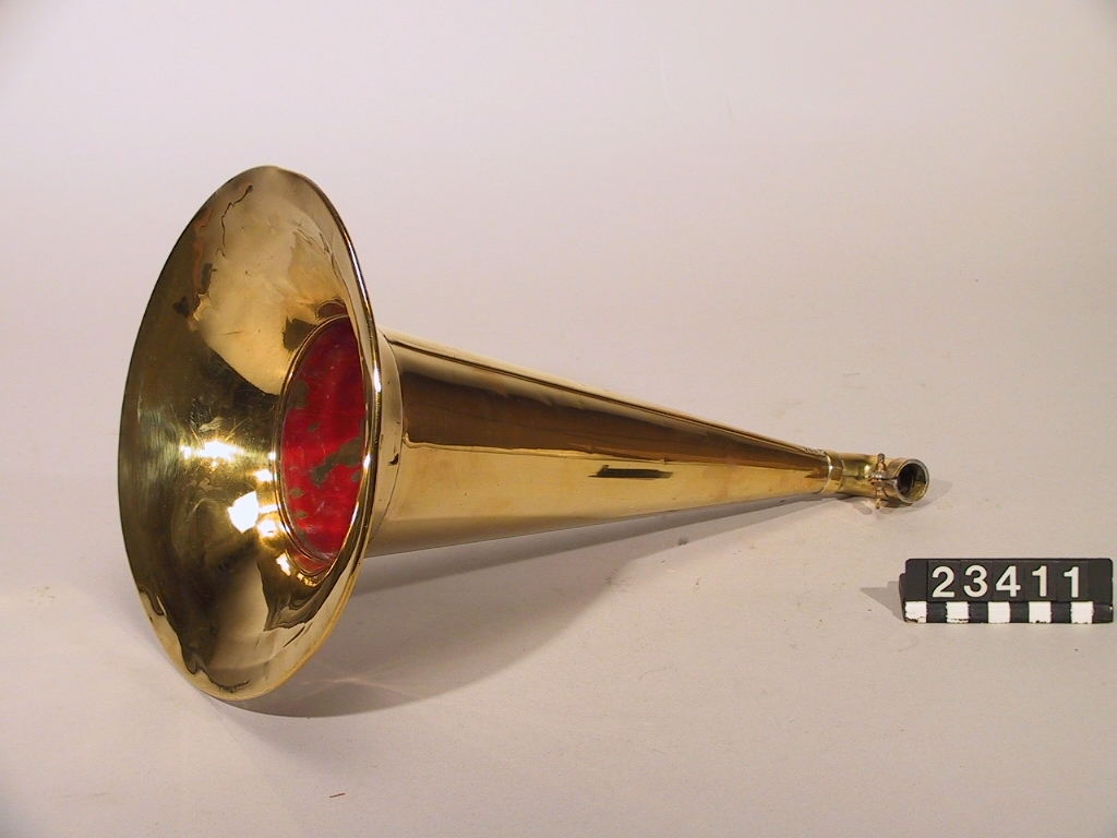 Grammofon av den första kommersiella typen. Bottenplattan märkt: DRP 45048. Tratt av mässing, stämplad: "1778". Trattmynningen stämplad med nummer "62". På insidan är tratten målad med röd färg. Trattens främre del skall vara riktad snett uppåt genom att den ligger på ett stöd som på detta exemplar saknas. Ingår även 1st. skiva