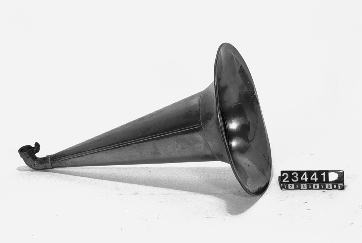 Grammofon av den första kommersiella typen. Bottenplattan märkt: DRP 45048. Tratt av mässing, stämplad: "1778". Trattmynningen stämplad med nummer "62". På insidan är tratten målad med röd färg. Trattens främre del skall vara riktad snett uppåt genom att den ligger på ett stöd som på detta exemplar saknas. Ingår även 1st. skiva