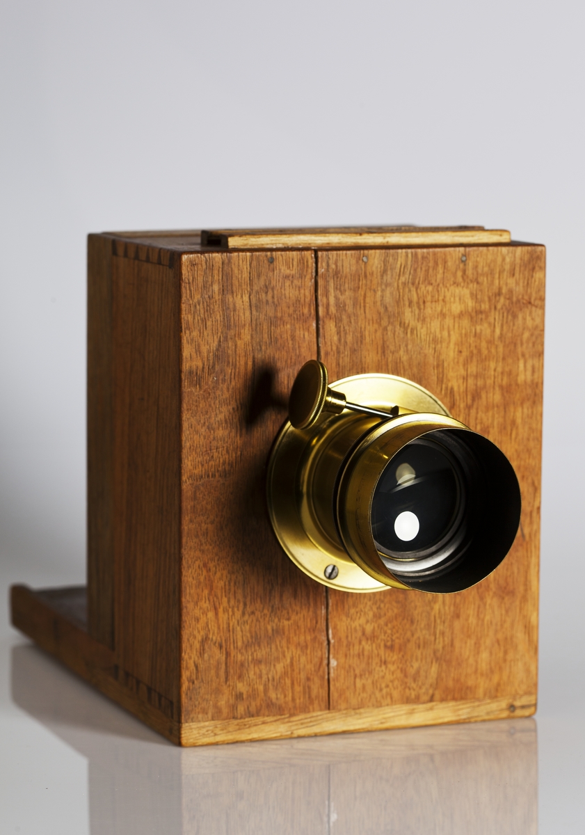 Kamera, skjutlådemodell. Våtplåt 9,5 x 11,5. Objektiv: Alexis Millet, Opticien Bte'SGDG 160r.st:Martin Paris. Nr 605. Utrustning för fotografering på resor, jämte koffert. Lösa delar: kamera av trä med objektiv från Alexis Millet, Paris, nr. 605, objektivlock av mässing, visirskiva, 4 kassetter för våtplåtar 9 x 12 cm, bakstycke med visirskiva för stereobilder 8 x 8 cm, 2 kassetter för stereovåtplåtar, kärl av zinkplåt med lock (gångjärnet avbrutet), trattformat kärl av zinkplåt, mindre kuvert av glas (spräckt och lagad, troligen av givaren), större kuvert av glas, torkställ av trä, 2 skivor av trä med spår för plåtar, kopieram för max 16 x 20 cm, vikbar skiva av trä (för beredning, troligen av våtplåtar), liten bordskiva med kantlist (passar till stativet TM 25.111,fodral av trä med 12 st. våtplåtnegativ 9 x 12 cm (porträtt och skulpturer), fodral av trä med 12 st. sämre negativ, fodral av trä med 10 st. blanka och  skrapade glasplåtar, diverse plåtar i paket (i ask ny 1950), fodral av trä med 11 st. stereovåtplåtar, varav 3 preparerade.
Tillbehör: Koffert.