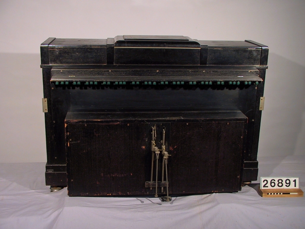 Pianotillsats för automatisk spelning på pianoklaviatur medelst perforerade notrullar av papper för pneumatisk verkan. Modell 1919. Märkt: Piano nr 14227, apparat nr 19422, verk nr 82947.
Tillbehör: Stol, svartlackerad.