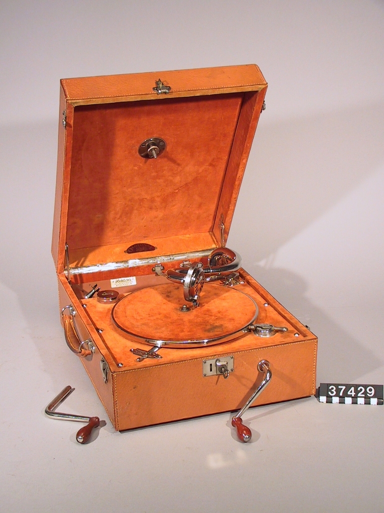 Resegrammofon, med fjäderverk, stiftdosa och hastighetsregulator. Läderklädd väska och förnicklade metalldelar.
Tillbehör: 2 vevar och nyckel.
