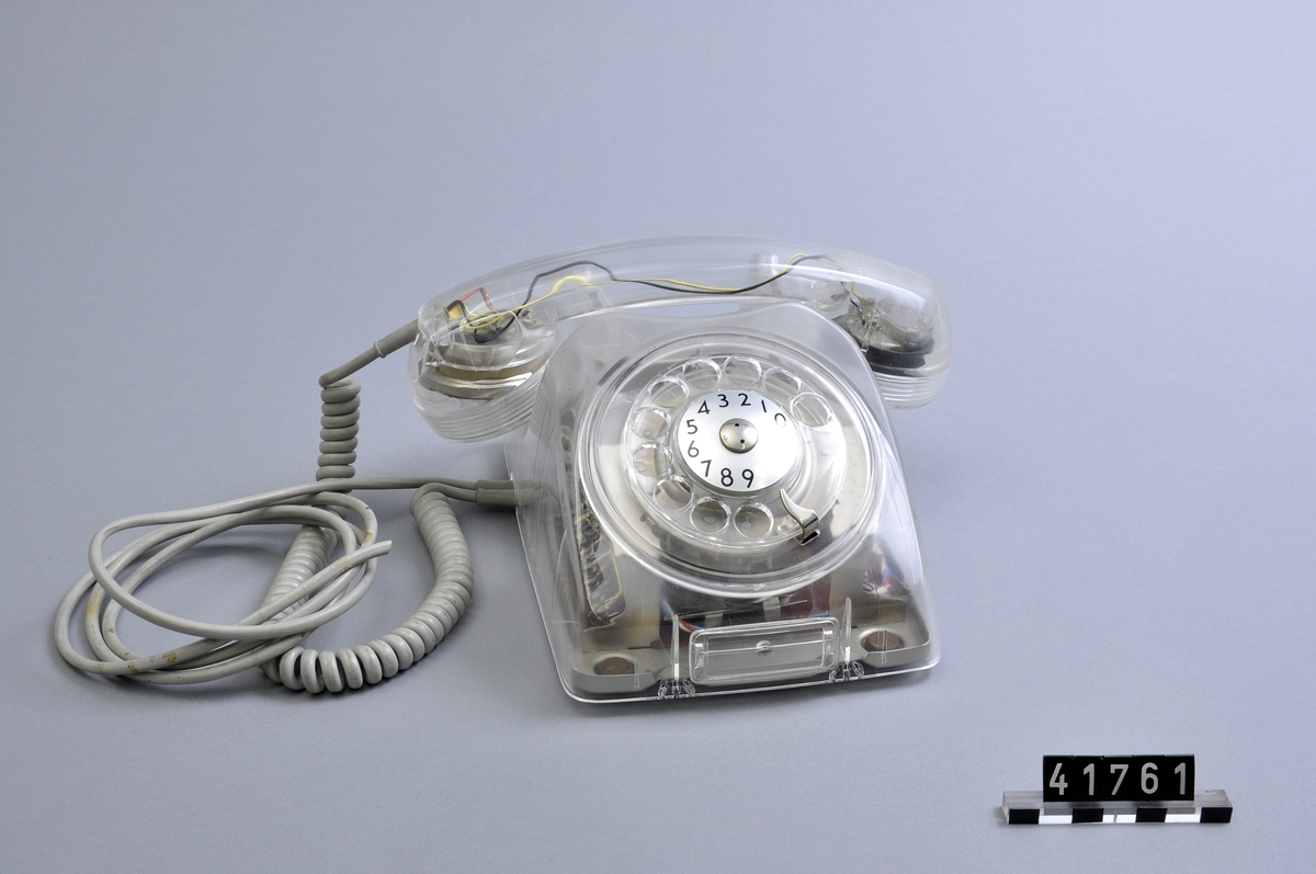 Telefonapparat Dialog för AT-system, huvudapparat, anknytningsapparat till växel och sidoapparat. Bordsmodell av genomskinlig termoplast med fingerskiva. Ringsignalens styrka är ställbar med ett reglage på apparatens undersida.