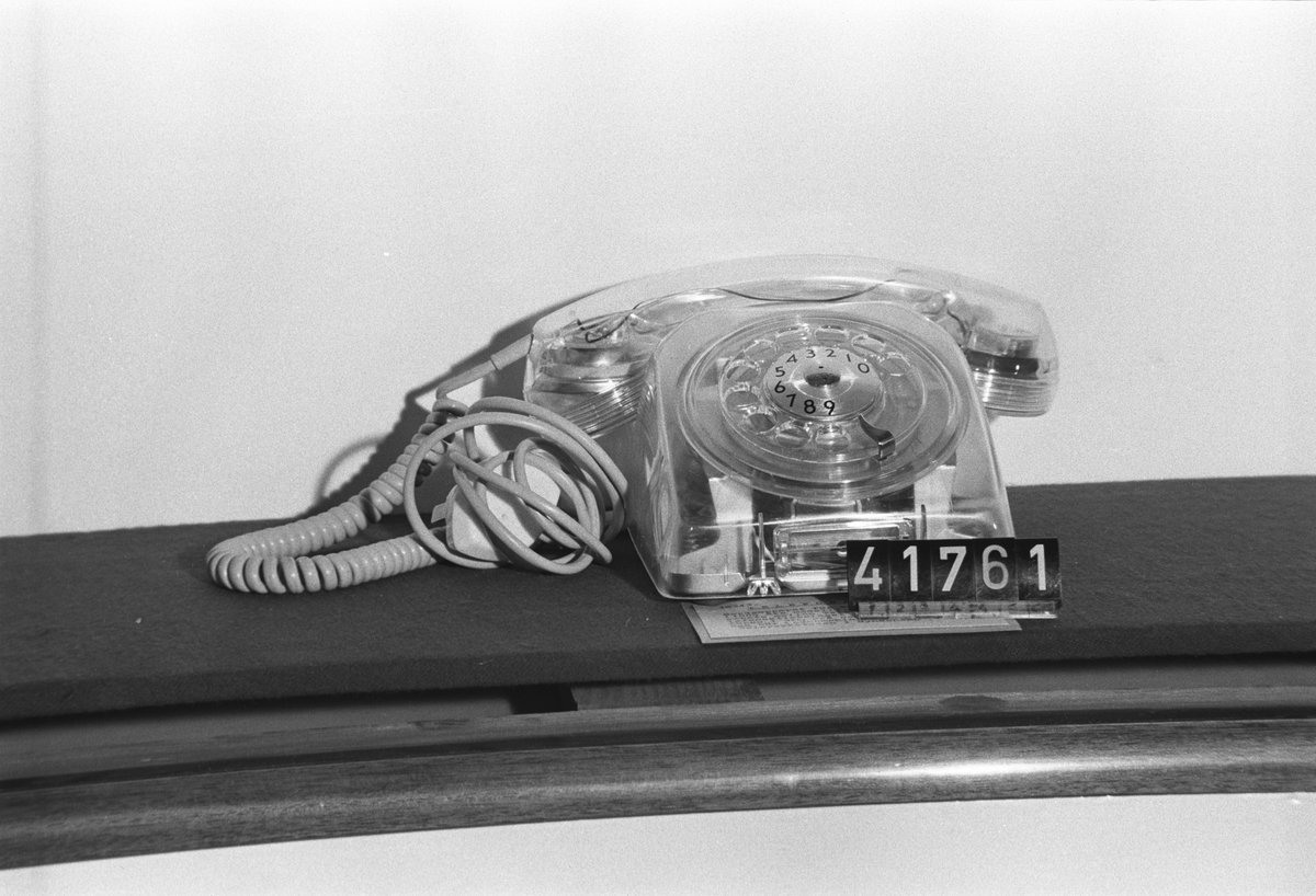 Telefonapparat Dialog för AT-system, huvudapparat, anknytningsapparat till växel och sidoapparat. Bordsmodell av genomskinlig termoplast med fingerskiva. Ringsignalens styrka är ställbar med ett reglage på apparatens undersida.