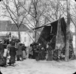 Skioptikonbild med motiv av folksamling vid marknadsstånd på Place de la Republique i Cusset, Frankrike.
Bilden har förvarats i kartong märkt: Vichy