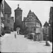 Skioptikonbild med motiv av torget Plönlein vid gatorna Kobolzellersteig och Spitalgasse.
Bilden har förvarats i kartong märkt: Rothenburg IV.