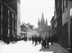 Skioptikonbild med motiv från Ansbach. Folkvimmel på okänd gata, i bagrunden syns kyrkan Kirche St. Gumbertus.