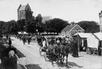 Torgmarknad i Båstad med stånd för försäljning av kläder. I bakgrunden Mariakyrkan.