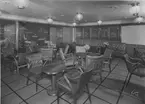 Ombord på M/S 1203 A Stockholm vid Svenska Amerika Linien, byggd i Moutalcone i Italien 1941. Turistklass röksalong med bar. Halvpanel i teak, övre delen målad ljust. Stolarna och sofforna klädda med omväxlande rött och brunt skinn. Målningen utförd av konstnärenGustaf Carlström. De dekorativa glasen i fönstret utförda av Ulla Skogh/AB Nybrofabriken, Fröseke.