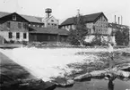 Morgårdshammars Mekaniska Verkstad. Nedanför fallet och intill Bergslagsälven ligga de äldsta verkstadsbyggnaderna med den gamla smedjan i mitten.