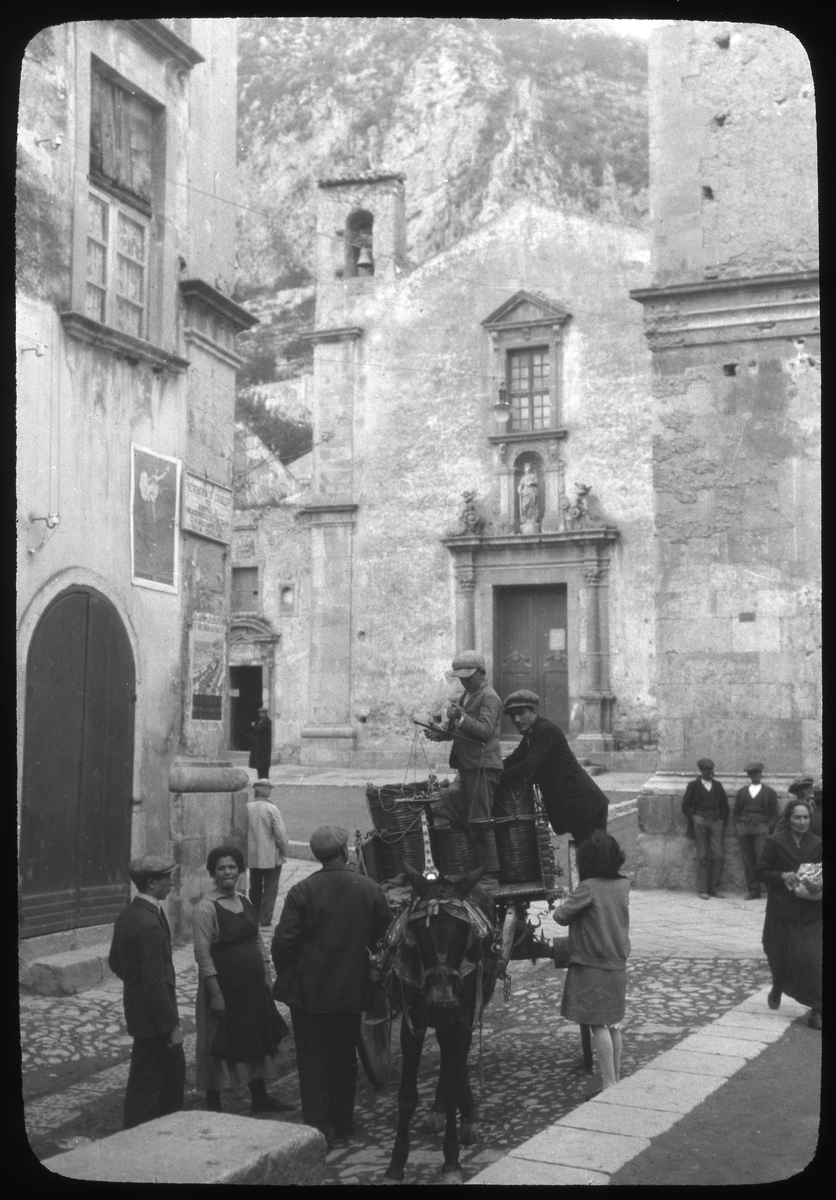 Skioptikonbild från institutionen för fotografi vid Kungliga Tekniska Högskolan. Bilden är troligtvis tagen i Taormina på Sicilien av John Hertzberg under en resa i Europa. Hertzberg blev docent i fotografi 1921vid Kungliga Tekniska Högskolan i Stockholm. Gatubild som visar pojkar på en kärra dragna av en åsna.