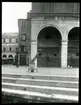 Skioptikonbild från institutionen för fotografi vid Kungliga Tekniska Högskolan. En man står på huvudet på öppen plats i Venedig. Bilden är troligen tagen av John Hertzberg under en resa i Europa.