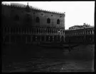 Skioptikonbild från institutionen för fotografi vid Kungliga Tekniska Högskolan. Motiv föreställande, till vänster i bild, Dogepalatset (Palazzo Ducale di Venezia) i Venedig . Bilden är troligen tagen av John Hertzberg under en resa i Europa.