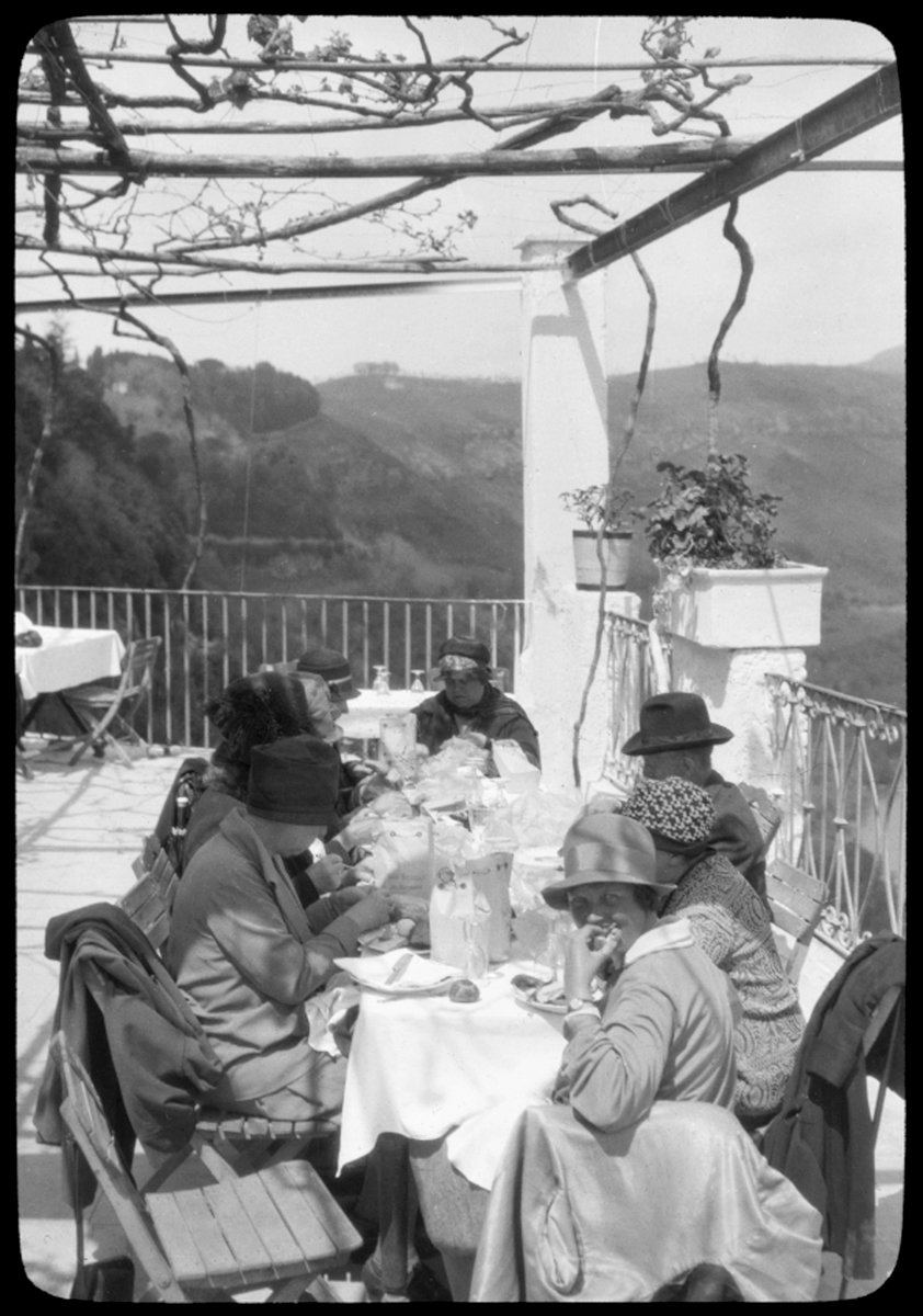 Skioptikonbild från institutionen för fotografi vid Kungliga Tekniska Högskolan. Motiv föreställande ett sällskap vid frukostbordet. Bilden är troligen tagen av John Hertzberg under en resa i Europa.