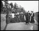 Skioptikonbild från institutionen för fotografi vid Kungliga Tekniska Högskolan. Motiv föreställande ett sällskap av kvinnor och män på landsväg. Femte person stående från höger är John Hertzberg.