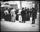 Skioptikonbild från institutionen för fotografi vid Kungliga Tekniska Högskolan. Motiv föreställande kvinnor, män och barn som lyssnar till något vid London Central Railway.. Bilden är troligen tagen av John Hertzberg under en resa i Europa.