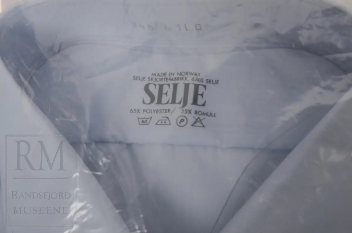 Jakke, bukse, slips, stasjonsmesterlue og skjorte.

a) Terylene, mørkeblå toskaftvevet. Fóret med svart kunstilke. Midtsøm i ryggen med splitt nederst, sidesømmer. Nedbrettet krage og slag. Enkeltspent med rette forkanter med 4 knapper med Norske løve i gult metall og knapphull. Utenpåsydde brystlommer med fold og knapping på klaff. Stikklommer med klaff. Tosømserme med 3 "Gull"-snorer. Rensemerke på innerlomme. Det er 3 innerlommer.

b) Langbukse med press uten oppbrett. Gylf med knapping. Linning med stolper til belte. 2 baklommer og 2 stikklommer. Nylon lomme- og linningsfór. 

c) Slips av blå kunstsilke. Knyttet. Fabrikkmerke "Derby Rhodia"

d): Skyggelue i svart ullstoff. Flat, rund pill. Plastskygge. Svetterem av brunt skinn. NSB emblem foran. Tre gullsnorer og rød snor i strikk. Rosett på gullsnor. Svart plastbånd festet med knapp på hver side. Fabrikkmerke.

e) Skjorte, lyseblå polyester og bomull fra Selje Skjortefabrikk. I plastpose. Ikke åpnet. Aldri brukt.