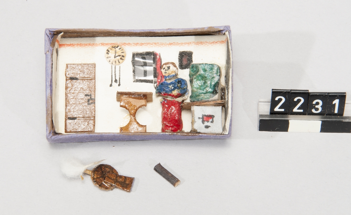 Asken märkt "Vulkan Sicherheits-Zünder", innehåller en leksaksmodell, föreställande ett rum med möbler samt en figur.