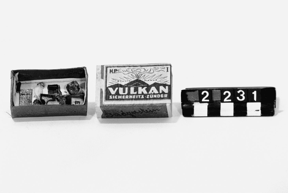 Asken märkt "Vulkan Sicherheits-Zünder", innehåller en leksaksmodell, föreställande ett rum med möbler samt en figur.