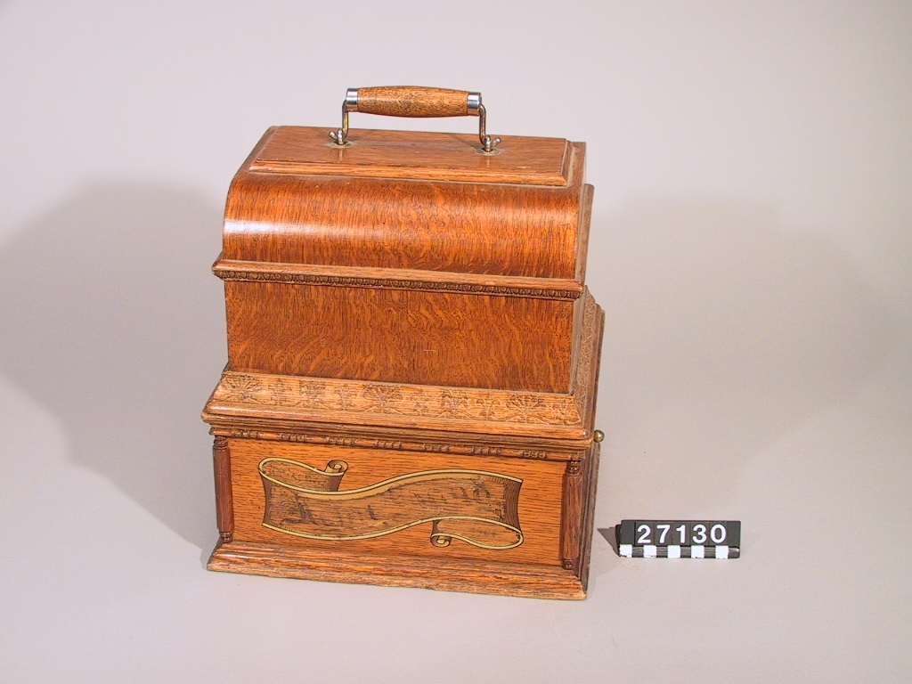 Fonograf, med svarvanordning. Avsedd för 5 tums vaxrullar, 120 varv/minut. Skylt: "The Graphophone patented May 4 1886 .... Mar 30 1897 Manufactured by the American Graphophone Company, New York, N.Y. Type HG 1216".
Tillbehör: Lösa delar: apparat, vev, ljuddosa för återgivning, ljuddosa för upptagning (båda i pappask), böjd tratt, huv av trä samt ytterhuv av brunt läder.