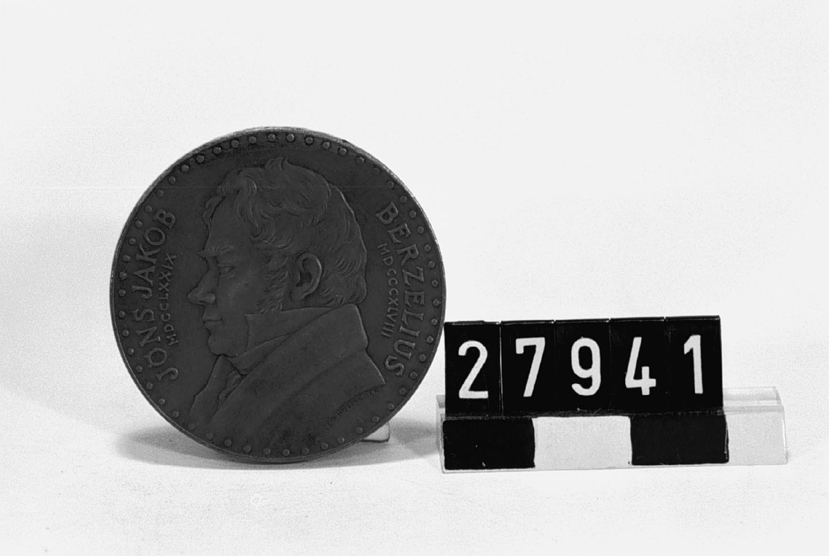 Medalj i brons över J J Berzelius (1779-1848), präglad till Tionde Nordiska Kemistmötet i Stockholm. 1959. Åtsidan: Porträtt, vänster profil, text vid sidorna: "Jöns Jakob MDCCLXXIX Berzelius MDCCCXLVIII". Frånsidan: Manlig genius, omgiven av kemiska laboratorieapparater samt beteckningar för vissa grundämnen enligt Berzelius system och reaktionsformler. Efter modell av skulptören Leo Holmgen.