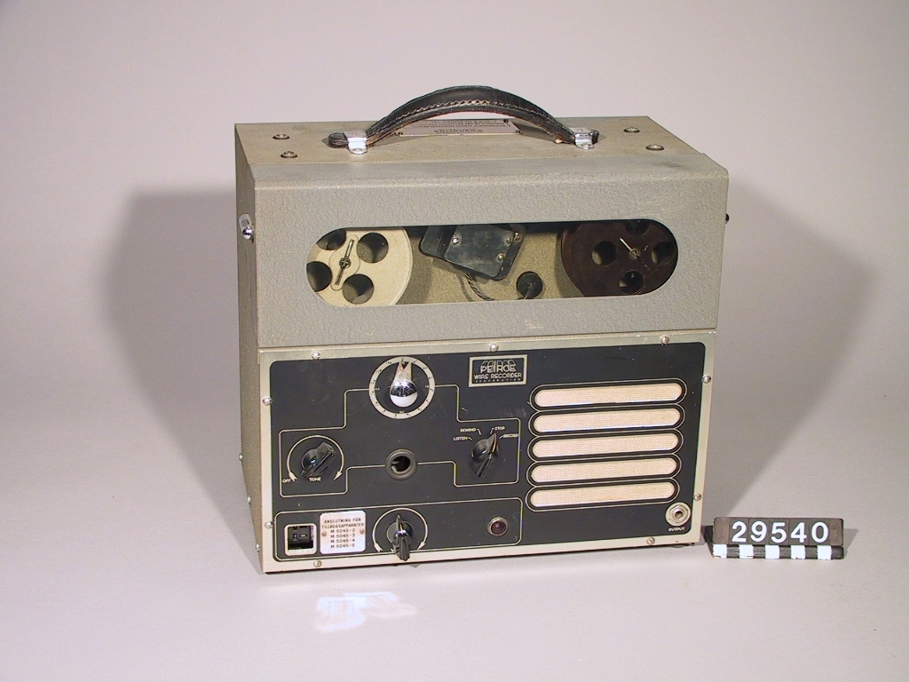 Trådspelare. Mikrofon och nättrafo separat. Förvaras i trälåda med bärhandtag. Tråddiktafonen är i 4 delar: 1 st. tråddiktafon, 1 st. bordsmikrofon (typ typ M 5040-2), 1 st. transformator och 1 st. trälåda. Tråddiktafonen har en 2 meter lång sladd för anslutning till transformatorn. Transformatorn har en 1 1/2 meter lång sladd för anslutning till elnätet. Bordsmikrofonen har en 4.8 meter lång sladd för anslutning till tråddiktafon. Lådans längd: 400 mm, bredd: 300 mm, höjd: 530 mm. Bordsmikrofonens längd: 140 mm, bredd: 95 mm, höjd: 190 mm. Tråddiktafonens längd: 340 mm, bredd: 195 mm, höjd: 290 mm. Transformatorns längd: 180 mm, bredd: 100 mm, höjd: 110 mm. Skylt: Bolinders tråd-diktafon M 4050-2.