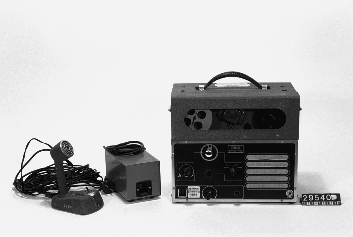 Trådspelare. Mikrofon och nättrafo separat. Förvaras i trälåda med bärhandtag. Tråddiktafonen är i 4 delar: 1 st. tråddiktafon, 1 st. bordsmikrofon (typ typ M 5040-2), 1 st. transformator och 1 st. trälåda. Tråddiktafonen har en 2 meter lång sladd för anslutning till transformatorn. Transformatorn har en 1 1/2 meter lång sladd för anslutning till elnätet. Bordsmikrofonen har en 4.8 meter lång sladd för anslutning till tråddiktafon. Lådans längd: 400 mm, bredd: 300 mm, höjd: 530 mm. Bordsmikrofonens längd: 140 mm, bredd: 95 mm, höjd: 190 mm. Tråddiktafonens längd: 340 mm, bredd: 195 mm, höjd: 290 mm. Transformatorns längd: 180 mm, bredd: 100 mm, höjd: 110 mm. Skylt: Bolinders tråd-diktafon M 4050-2.