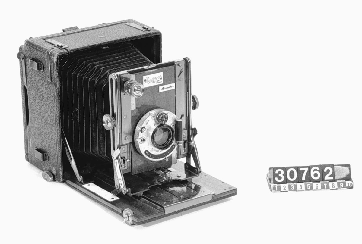 Klappkamera för planfilm och glasplåtar i svart läder, bärbar med handrem avsedd även för stativupphängning. För 9 x 12 cm planfilm med Koilos slutare. Slutare: Koilos 11:300 sek. Objektiv: Voigtländer Collinear III. Brännvidd: 15 Com. Ljusstyrka: 1:6,8. Glasp. form, längd: 45 mm.