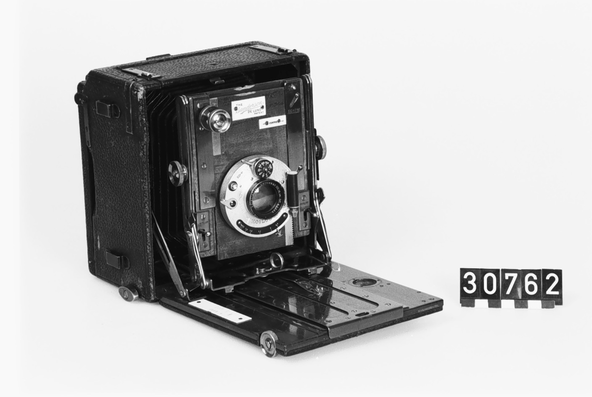 Klappkamera för planfilm och glasplåtar i svart läder, bärbar med handrem avsedd även för stativupphängning. För 9 x 12 cm planfilm med Koilos slutare. Slutare: Koilos 11:300 sek. Objektiv: Voigtländer Collinear III. Brännvidd: 15 Com. Ljusstyrka: 1:6,8. Glasp. form, längd: 45 mm.