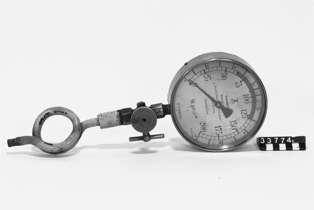Manometer. Märkt N.A.F. Graderad 0-200 kg/tum och 0-14 1b/kv. cm2. Monterad på expanderslinga av stålrör 175 mm högt med kran av mässing.