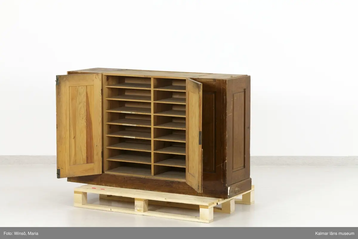 KLM 45471:1-2. Hurts, skrivbordshurts. Två stycken. Avlång hurts utan överdel. Av trä, ådringsmålad i ljusbrun kulör. Hurts :1 har på vardera kortsida en dörr med inbyggt lås. Inuti utrymmena diverse fack och hyllor. På ena långsidan en dubbeldörr med inbyggt lås. Utrymmet är indelat i två fack och åtta hyllplan. På några av hyllplanens främre kant är skrivet: Normal-skrivpapper, Skrivpapper 375x480, Postpapper 47 ark, Läskpapper 8 ark. Hurts :2 har på vardera kortsida utdragbara lådor, ett flertal saknas. Båda hurtsarna är försedda med spegeldörrar/väggar.