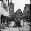 Skioptikonbild med motiv av hovslagare vid smedja i Rothenburg.
Bilden har förvarats i kartong märkt: Rothenburg V. 1902