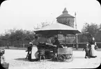 Skioptikonbild med motiv av marknadsstånd på torg i Nürnberg, bakom skymtar ett av tornen i stadsmuren.
Bilden har förvarats i kartong märkt: Nürnberg IX. 1901. Text på bild: 