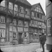 Skioptikonbild med motiv av man som betraktar ett äldre hus, Hannoversch-Münden.
Bilden har förvarats i kartong märkt: Resan 1904. München