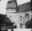 Skioptikonbild med motiv av kvinna vid St. Wolfgangs kapelle, St. Wolfgangs Kirche, Rothenburg.
Bilden har förvarats i kartong märkt: Vårresan 1910. Rothenburg. XXVIII.. Text på bild: 