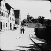 Skioptikonbild med motiv kvinna och ung man strosande på gata i Rothenburg.
Bilden har förvarats i kartong märkt: Vårresan 1910. Rothenburg. XXVIII.