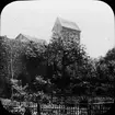 Skioptikonbild med motiv av Turm der Stadtmauer med trädgård, Fradungen.
Bilden har förvarats i kartong märkt: Vårresan 1910. Fladungen 7. X.