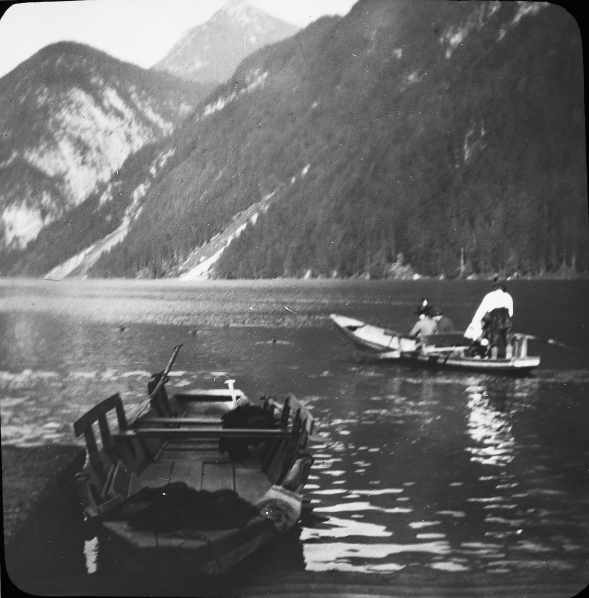 Skioptikonbild med motiv av båtar på fjällsjön Königssee i sydöstra Bayern.
Bilden har förvarats i kartong märkt: Höstresan 1909.Köningssee 3. München 1. Innsbruck 3. No: 13. Text på bild: "Am Köningssee".