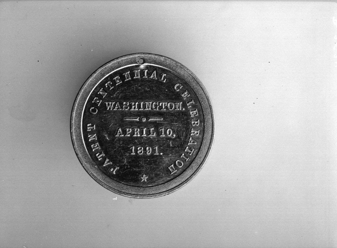 Har tillhört Gustaf de Laval. Slagen till minne av amerikanska patentverkets 100-årsjubileum år 1891. Åtsidan: Örn och diverse emblem med text runtom: "PATENT OFFICE UNITED STATES OF AMERICA". Frånsidan: "PATENT CENTENNIAL CELEBRATION, WASHINGTON APRIL 10. 1891". Tjocklek 40 mm.