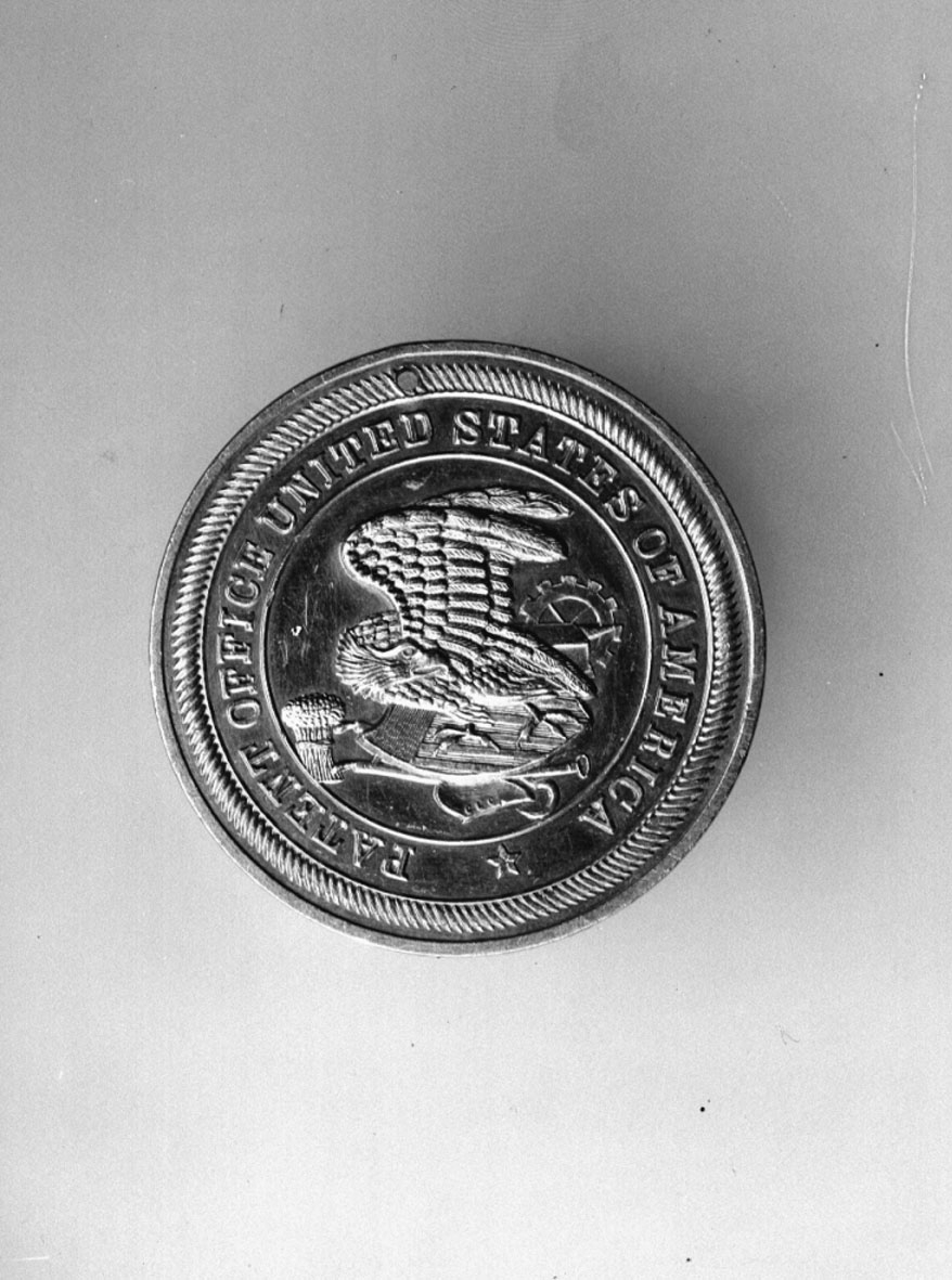 Har tillhört Gustaf de Laval. Slagen till minne av amerikanska patentverkets 100-årsjubileum år 1891. Åtsidan: Örn och diverse emblem med text runtom: "PATENT OFFICE UNITED STATES OF AMERICA". Frånsidan: "PATENT CENTENNIAL CELEBRATION, WASHINGTON APRIL 10. 1891". Tjocklek 40 mm.