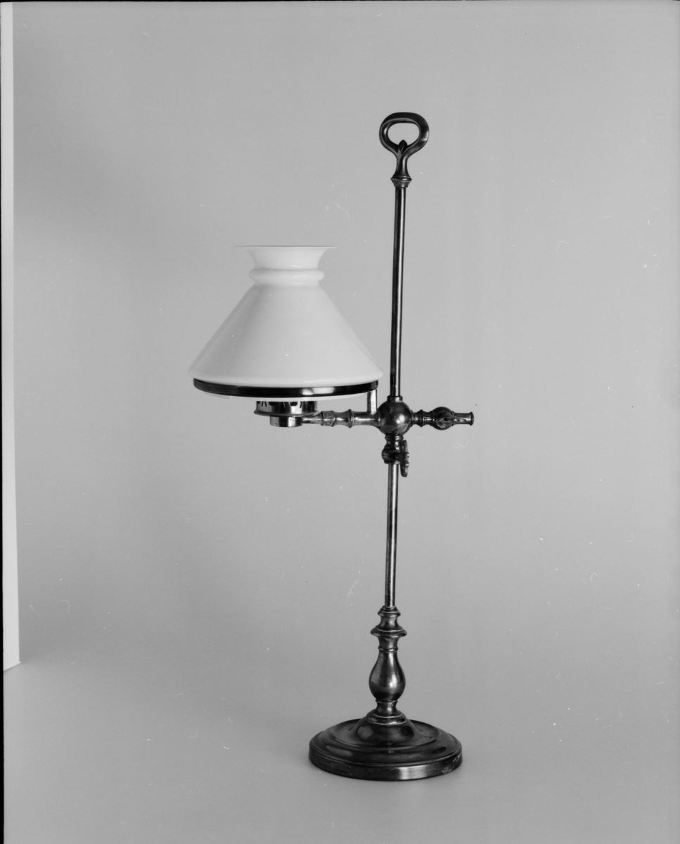 Bordslampa med höj- och sänkbar brännare av porslin samt lampkupa och kupring. Lampkupa: TM 18.136. En flisa borta ur kupans nedre hals. Lampglas saknas dock.
Tillbehör: Lösa delar: lampfot, kupring, lampkupa.