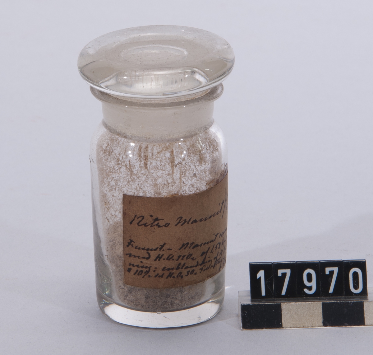 Prov på nitromannit, troligen sprängämne, i glasburk med etikett: "Nitro-Mannit (C6H8/NO3/6) Framst.-Mannit sammanrifs med HONO2 af 1.52 sp.v. till lösning: en blandning af 4 Â« d l HONO2 & 10 Â« H2 O4 SO4 tillsättes de Laval 1876".